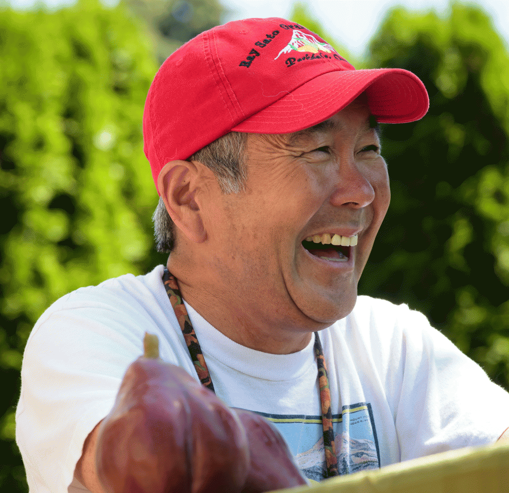 Pear grower Gordy Sato in a red hat laughing